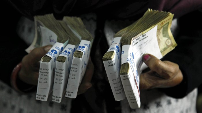 FILE - In this Dec. 16, 2011 file photo, a cashier holds bundles of Indian rupee bank notes at a bank in Allahabad, India. India's prime minister has announced late Tuesday, Nov. 8, 2016, scrapping of high denomination 500 and 1,000 Indian rupees currency notes in what he describes as a major step to fight the menace of black money, corruption and fake currency. Prime Minister Narendra Modi in a speech carried live on radio and television on Tuesday says there is no need to panic as people would be able to deposit these currency notes in their bank account until December 30. (AP Photo/Rajesh Kumar Singh, File)