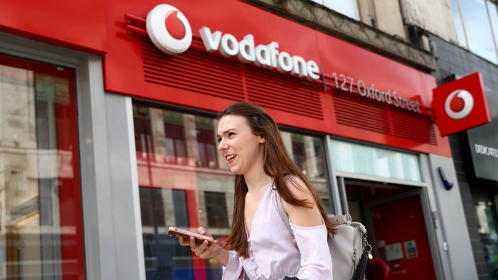FILE PHOTO: A woman holds a phone as she passes a Vodafone store in London, Britain May 16, 2017. REUTERS/Neil Hall/File Photo