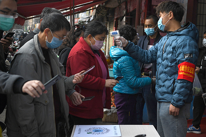 People wearing face masks scan a QR code to submit their personal information while security volunteers check their temperatures at an entrance of a grocery market, as the country is hit by an outbreak of the novel coronavirus, in Kunming, Yunnan province, China February 24, 2020. REUTERS/Stringer CHINA OUT. - RC268F9T0QX1