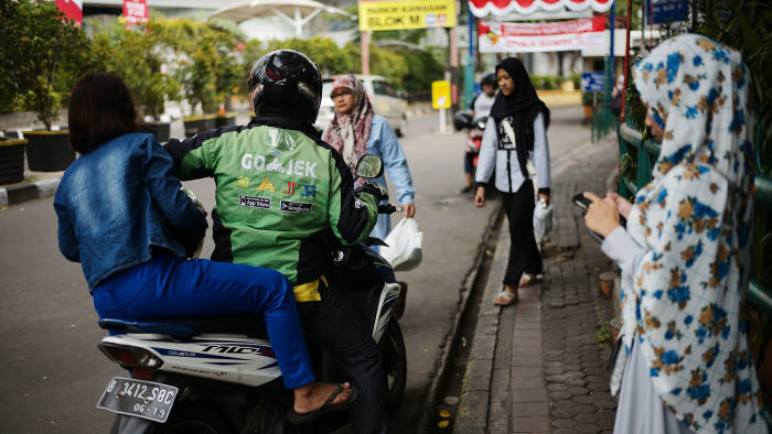 A Go-Jek motorcycle driver drops off a passenger in Jakarta, Indonesia, on Sunday, Aug. 13, 2017. President Joko Widodo is seeking hundreds of billions of dollars to finance an ambitious infrastructure agenda and to boost growth to 7 percent. Photographer: Dimas Ardian/Bloomberg