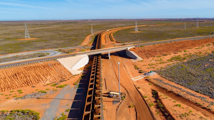 Freight wagons filled with iron ore travel under a highway in this aerial photograph taken near Port Hedland, Australia, on Wednesday, March 20, 2019. A two-day drive from the nearest big city, Perth, Port Hedland is the nexus of Australia’s iron-ore industry, the terminus of one of Australia’s longest private railways that hauls ore about 400 kilometers (250 miles) from the mines of BHP Group and Fortescue Metals Group Ltd. The line ran a record-breaking test train weighing almost 100,000 tons that was more than 7 kilometers long in 2001, and even normal trains haul up to 250 wagons of ore. Photographer: Ian Waldie/Bloomberg