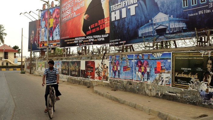 A cyclist rides past billboards and a wall plastered with posters of Bollywood movies in Mumbai on May 18, 2011.