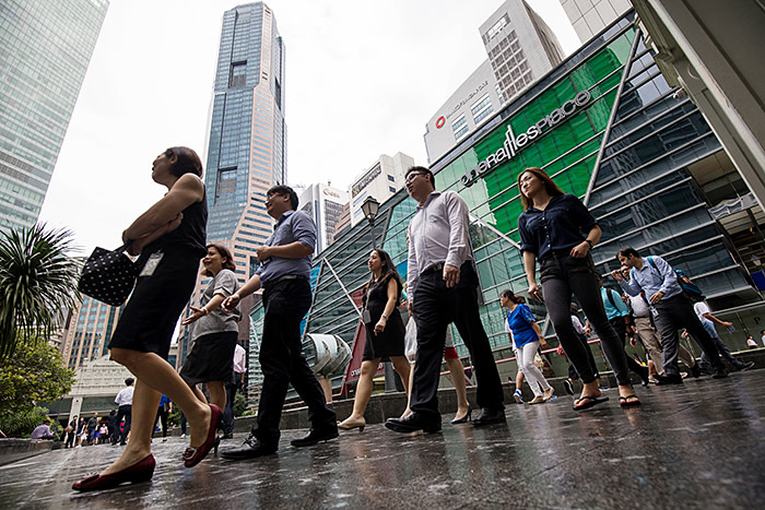 People walk past commercial buildings in the central business district of Singapore, on Wednesday, June 13, 2018. Tourism as well as the consumer sector will likely see a lift thanks to the influx of international media at the recent DPRK-USA Summit, according to RHB Research Institute Singapore Pte. Photographer: SeongJoon Cho/Bloomberg