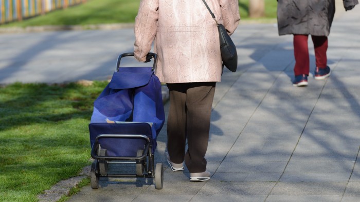 image of elderly woman with a bag on wheels on the street, rear view