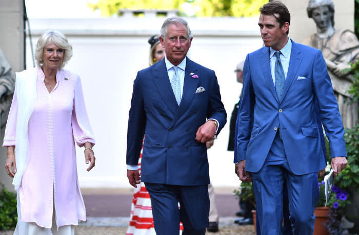 ***Retouched to defocus lady in red in background (L-R) Britain's Camilla, Duchess of Cornwall, Britain's Prince Charles, Prince of Wales and Ben Elliot arive for a reception in support of the Elephant family, a charity set up by Mark Shand, the Duchess of Cornwall's brother in London on June 30. 2015. The event called Travels to my Elephant will see painted rickshaws auctioned to raise money for Asian Elephants and later this year taking part in a race across Madhya Pradesh in India. AFP PHOTO / BEN STANSALL (Photo by BEN STANSALL / AFP)