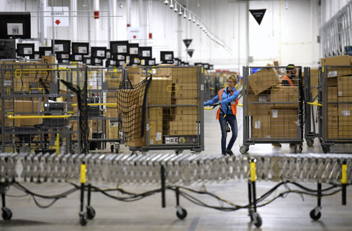 FILE - In this Friday, March 23, 2018, file photo, associates move bins filled with products at the loading dock of Amazon's then-new fulfillment center in Livonia, Mich. Amazon said Monday, March 16, 2020 that it needs to hire 100,000 people across the U.S. to keep up with a crush of orders as the coronavirus spreads and keeps more people at home, shopping online. (Todd McInturf/Detroit News via AP)