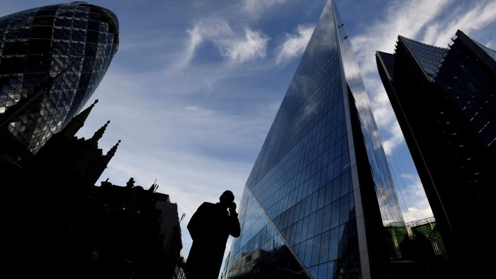 A man speaks on his phone as he walks past The Gherkin and other office buildings in the City of London, Britain November 13, 2018. REUTERS/Toby Melville - RC144545D070