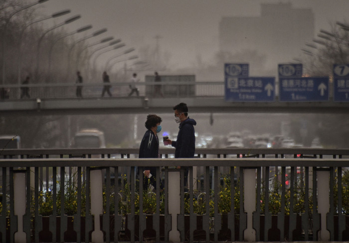 Pedestrians wear masks to protect themselves from unusually high levels of dust as they walk on an overpass during in Beijing on March 28, 2018. / AFP PHOTO / WANG ZHAO (Photo credit should read WANG ZHAO/AFP/Getty Images)