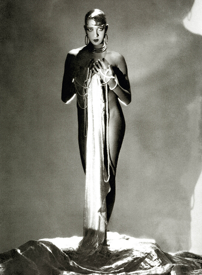 Dancer Josephine Baker, standing nude, with a long piece of fabric draped in front of her hanging from long stands of pearls which are wrapped around her hands. (Photo by George Hoyningen-Huene/Condé Nast via Getty Images)