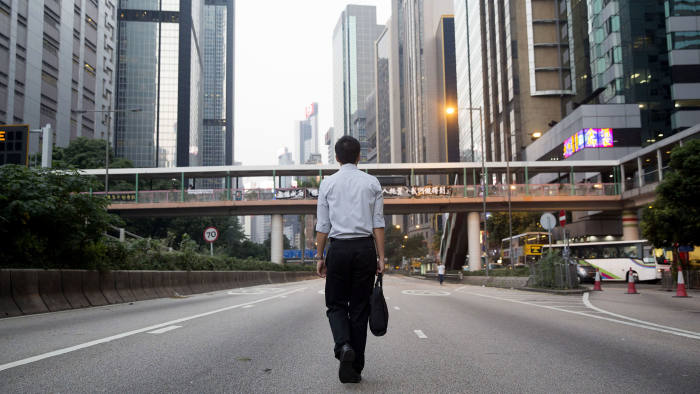 FILE PHOTO: A commuter walks on Gloucester Road, closed to traffic, near the Central Government Offices in Hong Kong, China, on Tuesday, Oct. 7, 2014. Hong Kong's protest leaders held a second round of talks with government officials, easing tensions in the streets as the city began to assess the impact of almost two weeks of demonstrations. Photographer: Brent Lewin/Bloomberg