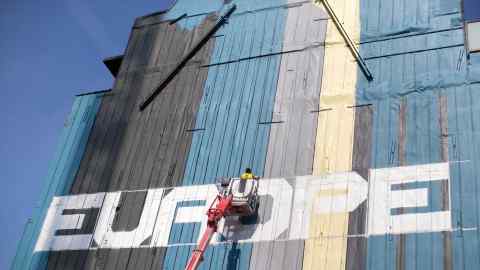 An artist stands on a cherry picker to work on a mural next to the European commission and the Europa building in Brussels, Belgium, on Thursday, June 22, 2017. EU leaders are expected to reaffirm their commitment to "robust" free trade and the Paris Agreement on climate change when the two-day meeting concludes on Friday. Photographer: Jasper Juinen/Bloomberg