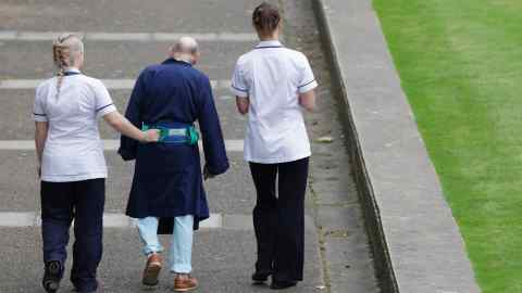 LONDON, ENGLAND - OCTOBER 13: Two NHS staff walk with an elderly patient outside St Thomas' Hospital on October 13, 2011 in London, England. Inspections carried out by the Care Quality Commission in England have found concerns in the standard of basic elderly care in over half the hospitals assessed. (Photo by Oli Scarff/Getty Images)