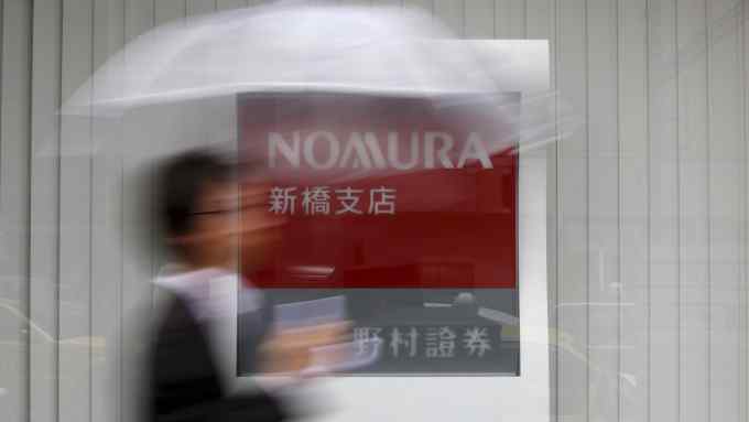 A man holding an umbrella walks in front of a signboard of Nomura Securities outside its branch in Tokyo October 29, 2013. REUTERS/Issei Kato/File Photo