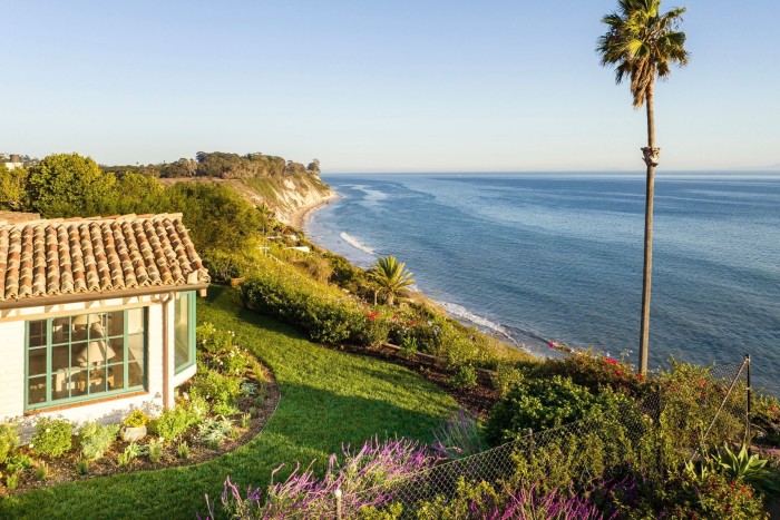 The front of a house on a bluff with a palm tree and sweeping views of the ocean, $9.995mn