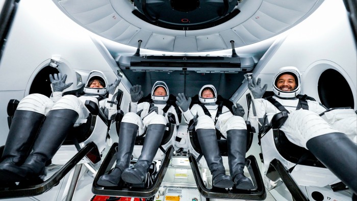 Four smiling astronauts seated in a space capsule