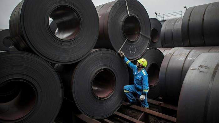 A worker inspects coils of steel in the storage yard of an ArcelorMittal plant
