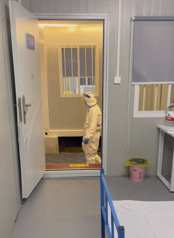 A member of staff in in the doorframe of Hale’s cabin, wearing a white hazmat suit and goggles