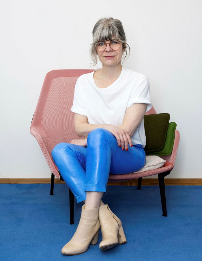A woman in white T-shirt and blue trousers sits on a pink chair