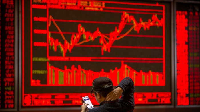 A Chinese investor uses his smartphone as he monitors stock prices at a brokerage house in Beijing