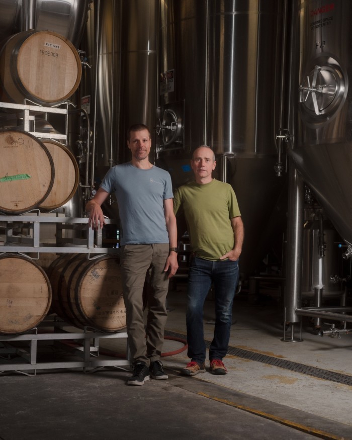 Iain Hill and Aaron Jonckheere of Strange Fellows Brewing standing by casks of beer and stainless-steel machinery