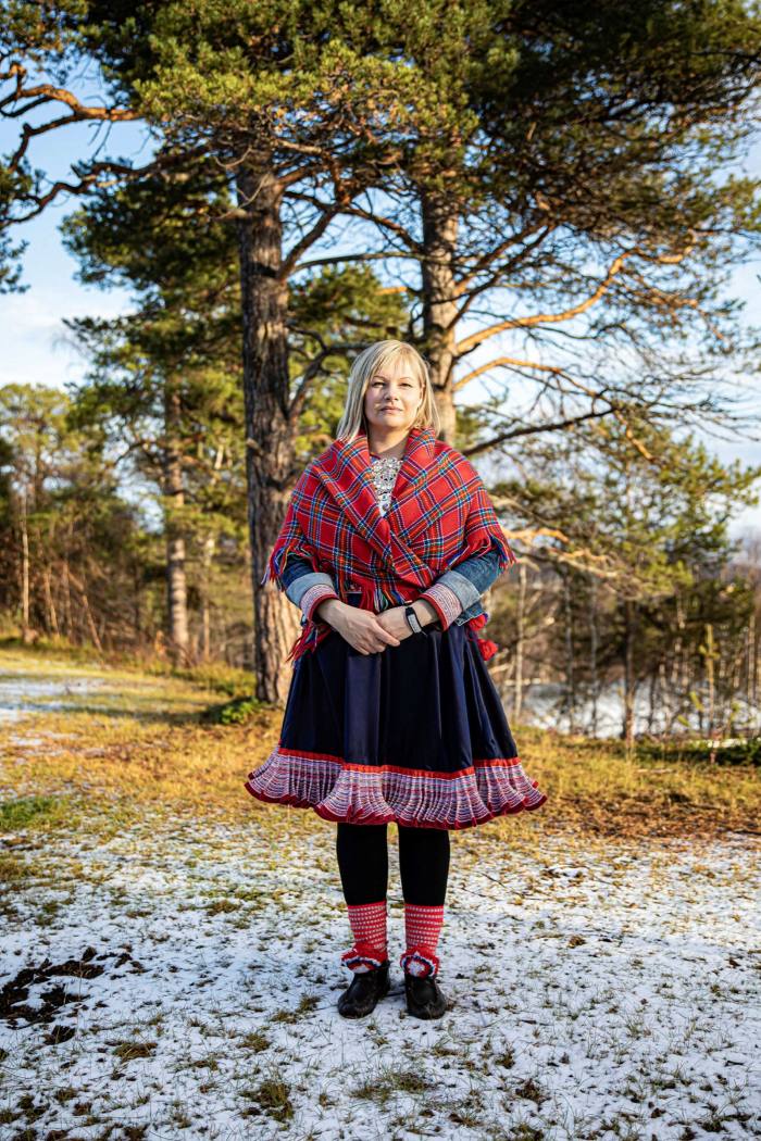 Artist Máret Ánne Sara in traditional Sami costume pictured standing on frosty ground with trees behind