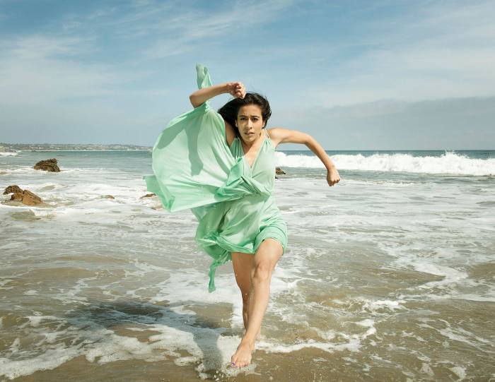 Photo of a person in a flowing green dress running through the surf on a beach