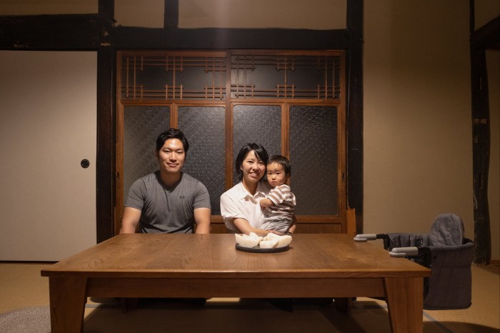 Kuranosuke’s mother holds him as she and his father sit smiling at a table in their home