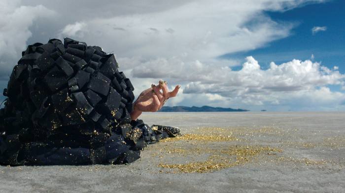 A hand reaches out from a large pile of charcoal on a gold-scattered plain