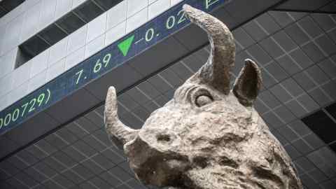 A sculpture of a bull stands as an electronic ticker board displays stock prices overhead at the Shenzhen Stock Exchange in Shenzhen, China