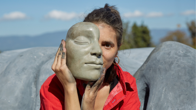 A woman hold a clay mask of a woman’s face over most of her face