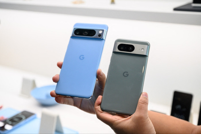 Two hands, one holding a Google Pixel 8 and the other holding a Google Pixel 8 Pro