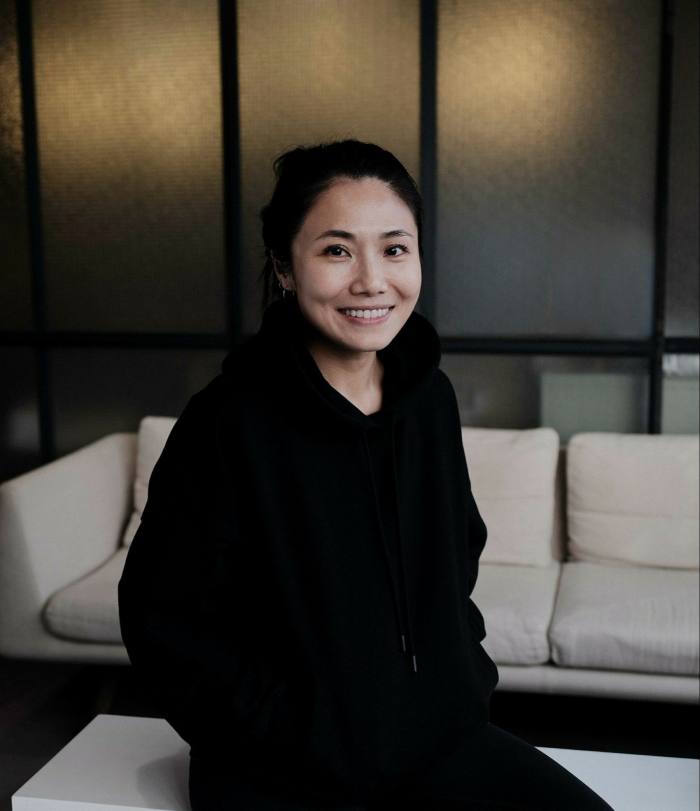 A woman sits on a table dressed in black and smiles at the camera
