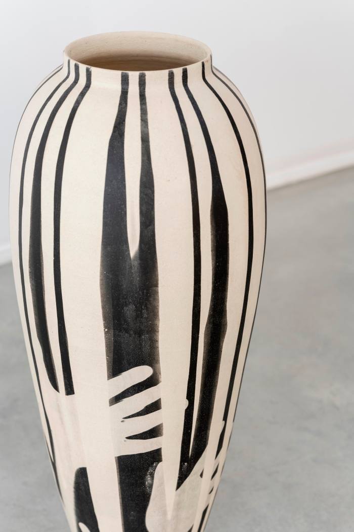 A tall ovoid-ish ceramic vase with black and white stripes and white handprints