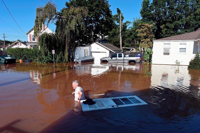 A man in waist-deep water walks by a door floating in floodwater 