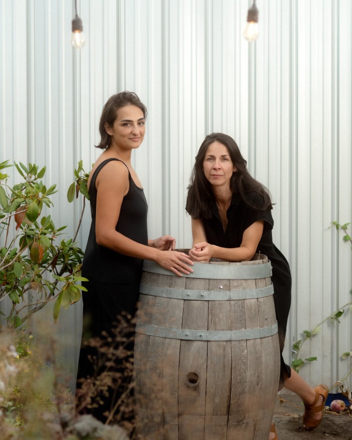 Anique Ross and Eleanor Stewart of Luppolo Brewing Company standing by a wooden cask in front of a corrugated iron wall