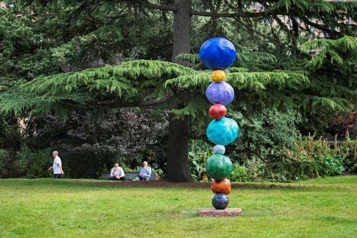A stacked sculpture of coloured balls in front of some trees