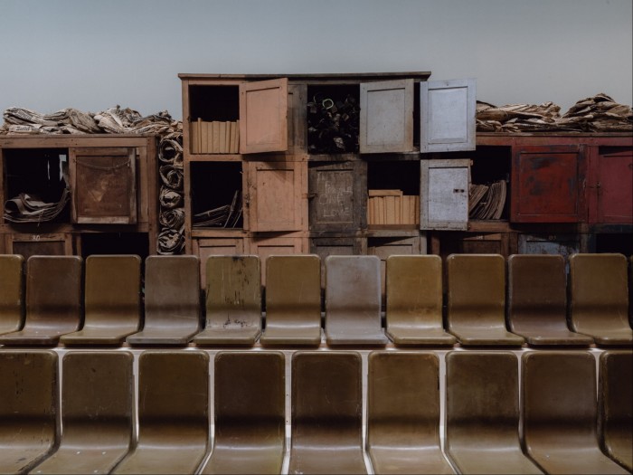 Wooden cabinets with papers tumbling out, in front of a row of plastic chairs 
