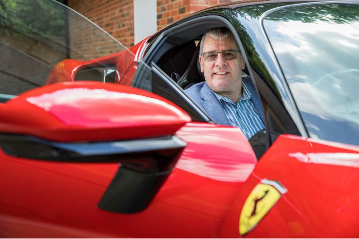 Graham Royle smailes at the camera from the driver’s seat of a red Ferrari with its door open