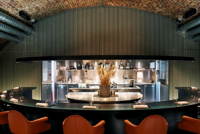Orange-red seating around a semi-circular black counter, behind which is a kitchen, at east London’s The Sea, The Sea