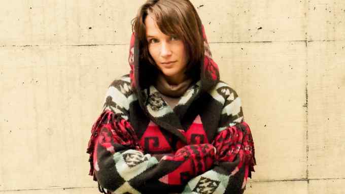 A portrait photo of Hélène Grimaud posing in a hooded cardigan with a blue, black and pink geometric pattern