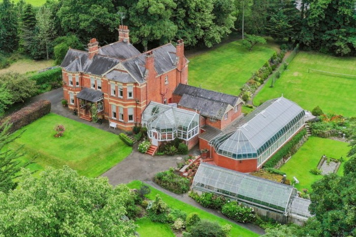 a large late-Victorian, red-brick country house seen from the air along with its outbuildings and landscaped grounds