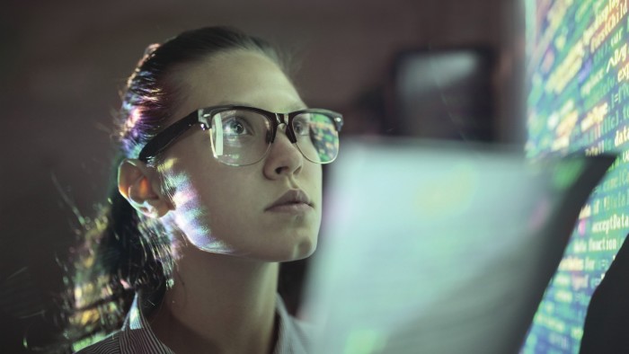 A woman looking up an electronic board, which is reflected on her eyeglasses