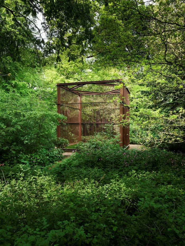 A large rust-coloured steel cage is set into the woods