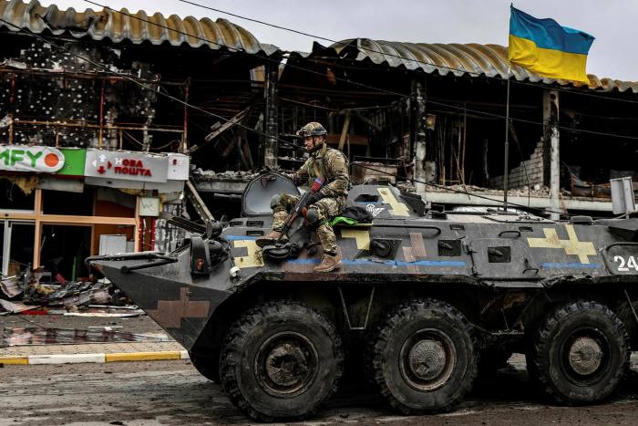 A Ukrainian soldier sits on top of a tank with a Ukrainian flag