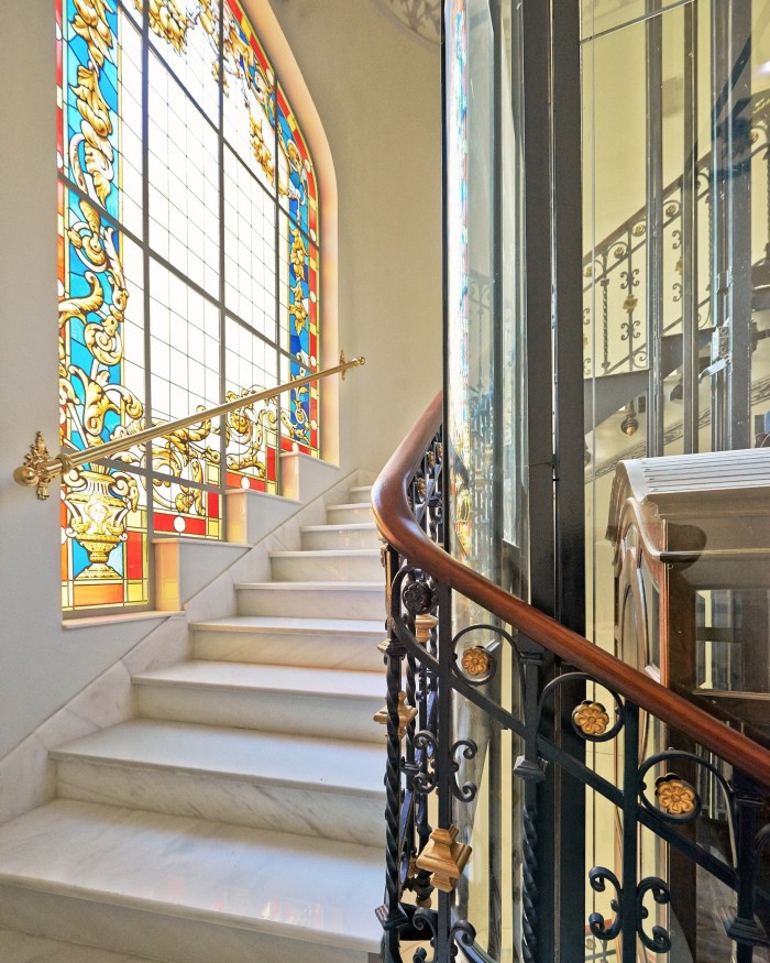 An early-20th-century stained-glass window on a staircase and the top of a restored old wrought-iron lift