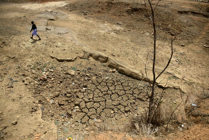An Indian farmer walks across the bed of a pond built under an Indian government scheme that has dried out during a water crisis