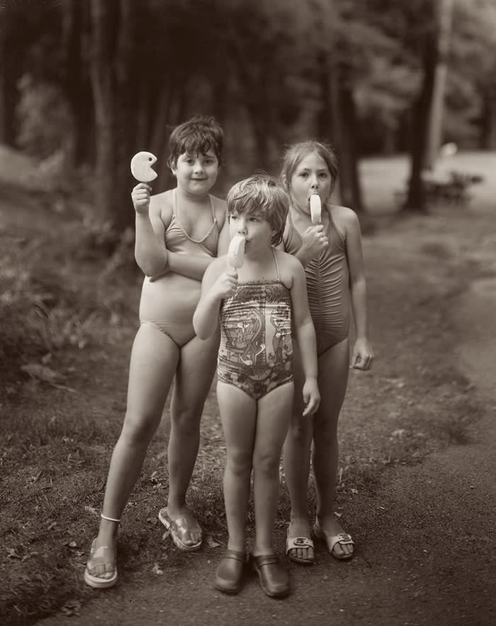 Three young girls in bathing suits stand eating ice cream bars