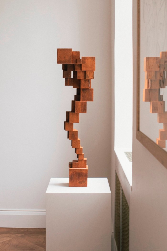 A blocky, Jenga-like semi-abstract sculpture of a figure carrying a box