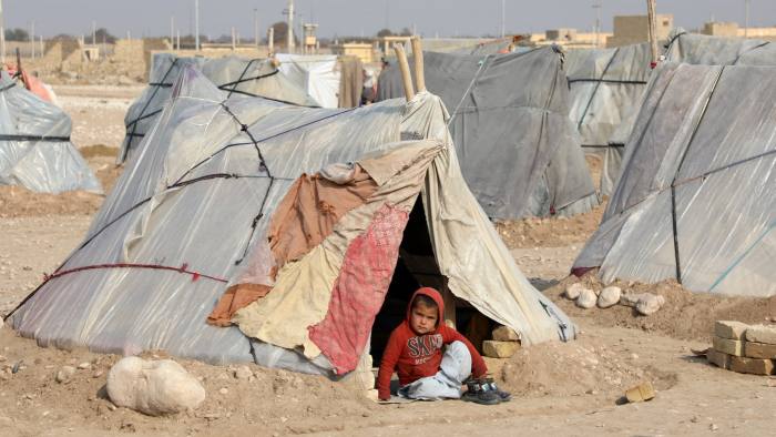 child refugee sitting outside a tent