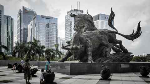 People stand in front of a sculpture of bulls at the entrance to the Shenzhen Stock Exchange building in Shenzhen
